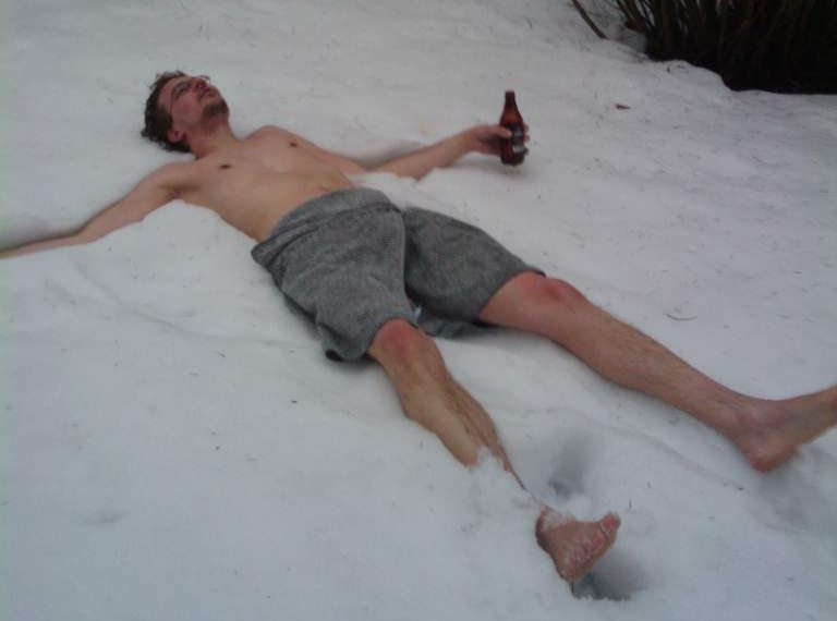 Image of amette lying in snow with only a towel and a beer